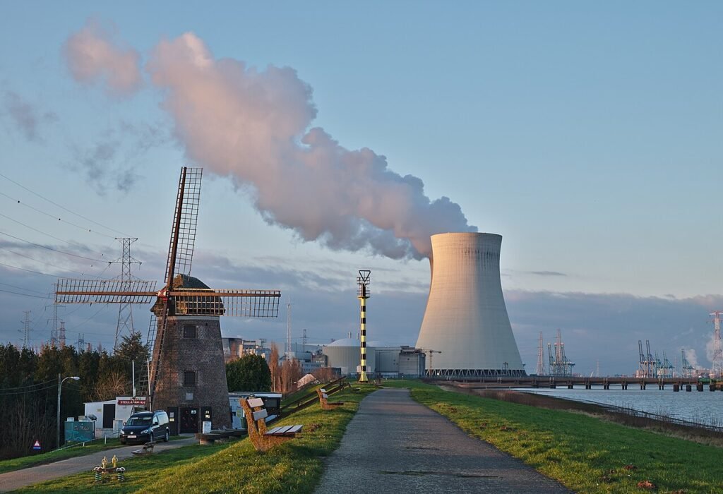 cooling tower of a power plant releasing smoke near a windmill showing industrial pollution and renewable energy contrast